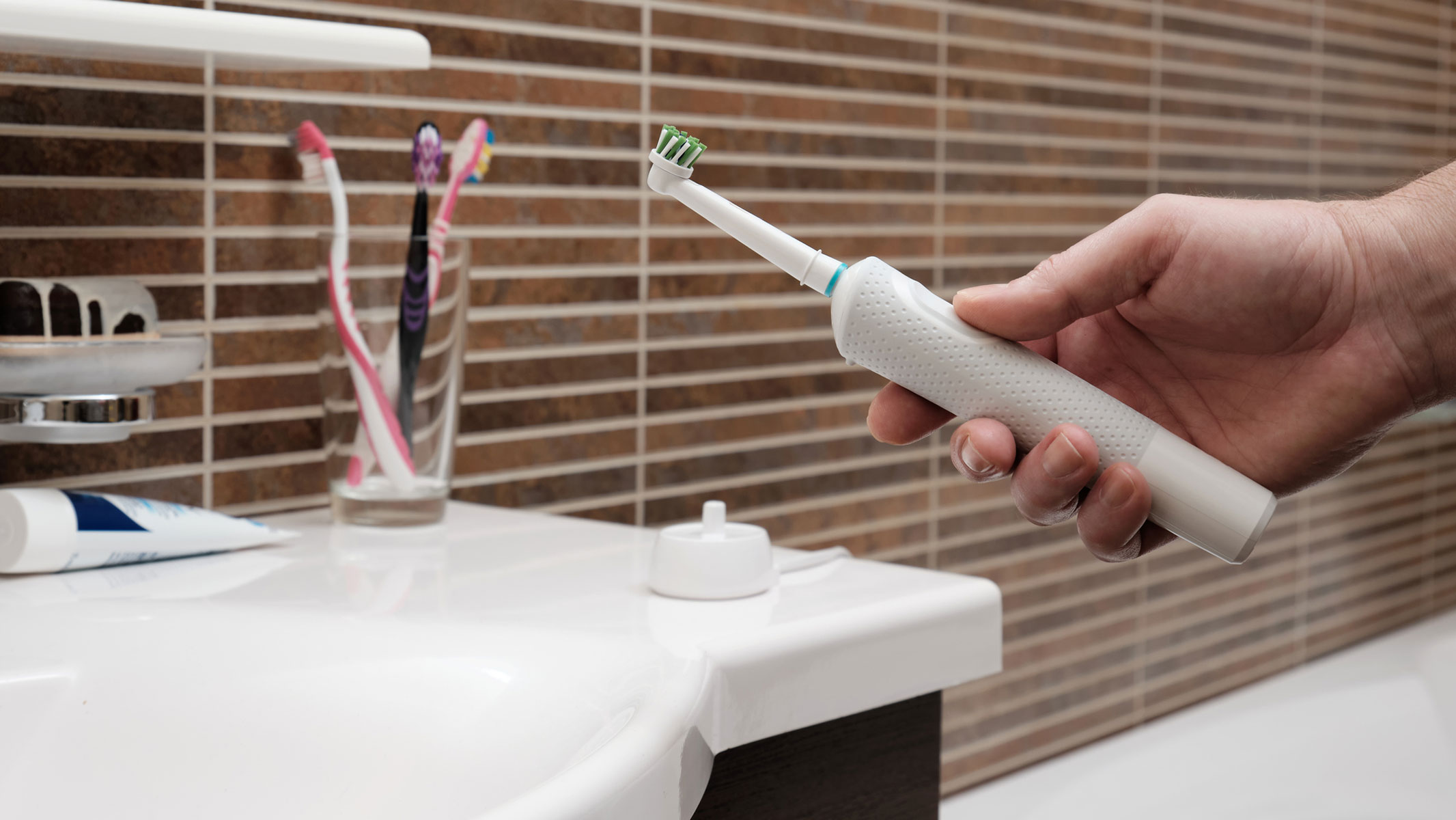 Close-up image of a man holding an electric toothbrush near the bathroom sink