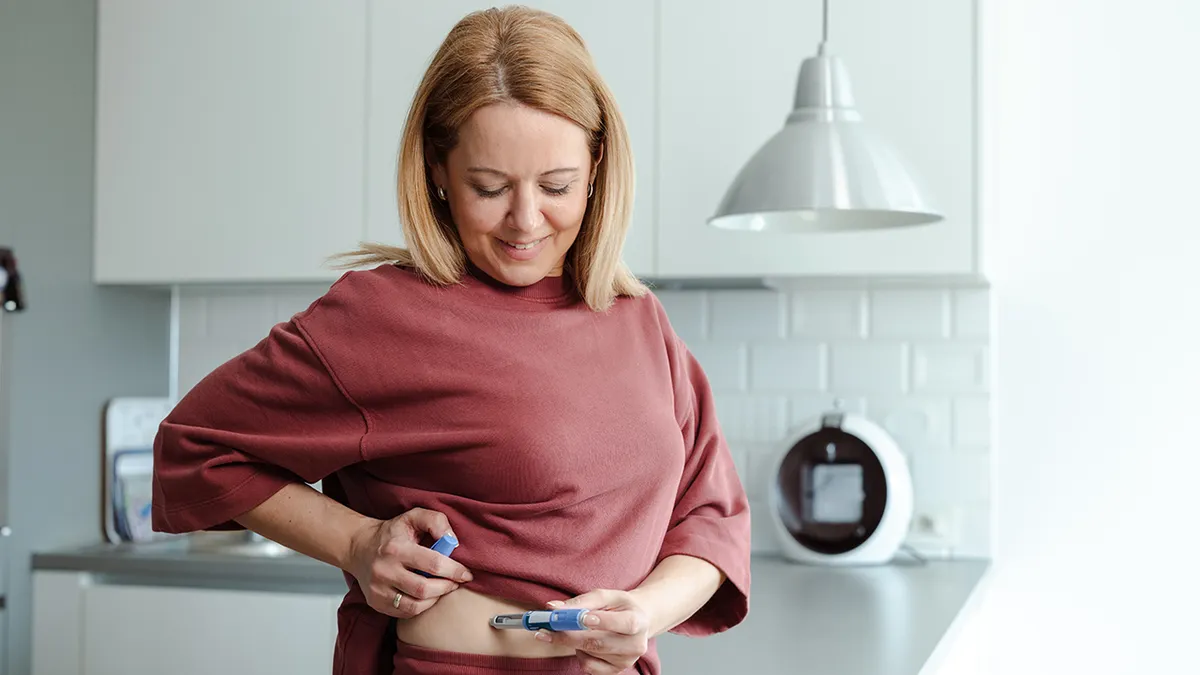 An adult woman performs an independent medical procedure in a home kitchen environment