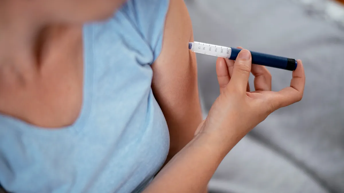 A woman in a blue T-shirt gives herself an injection of GLP-1 in the arm