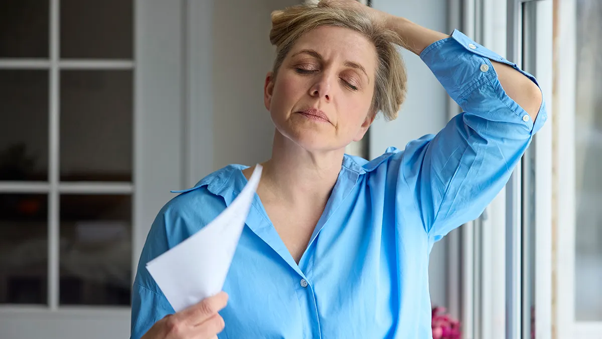 A menopausal woman cools herself at home during a hot flash by fanning with paper.