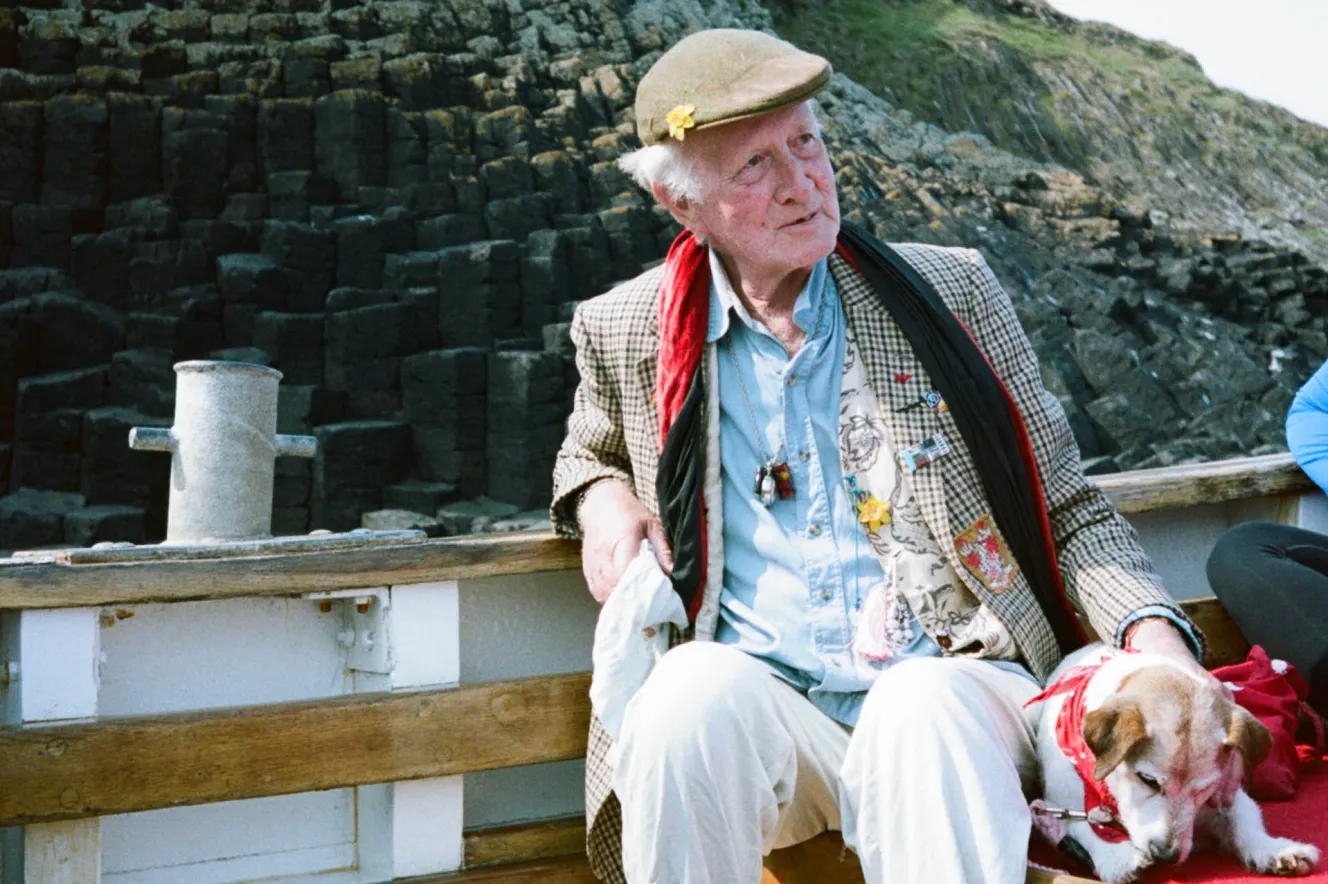 Peter Monro in a boat with a dog, with a cliffside in the background.
