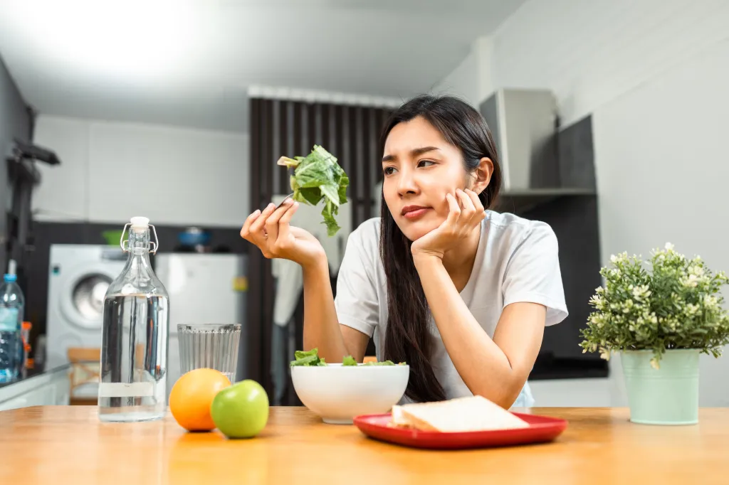 A young woman looking bored or unhappy in a forkful of salad