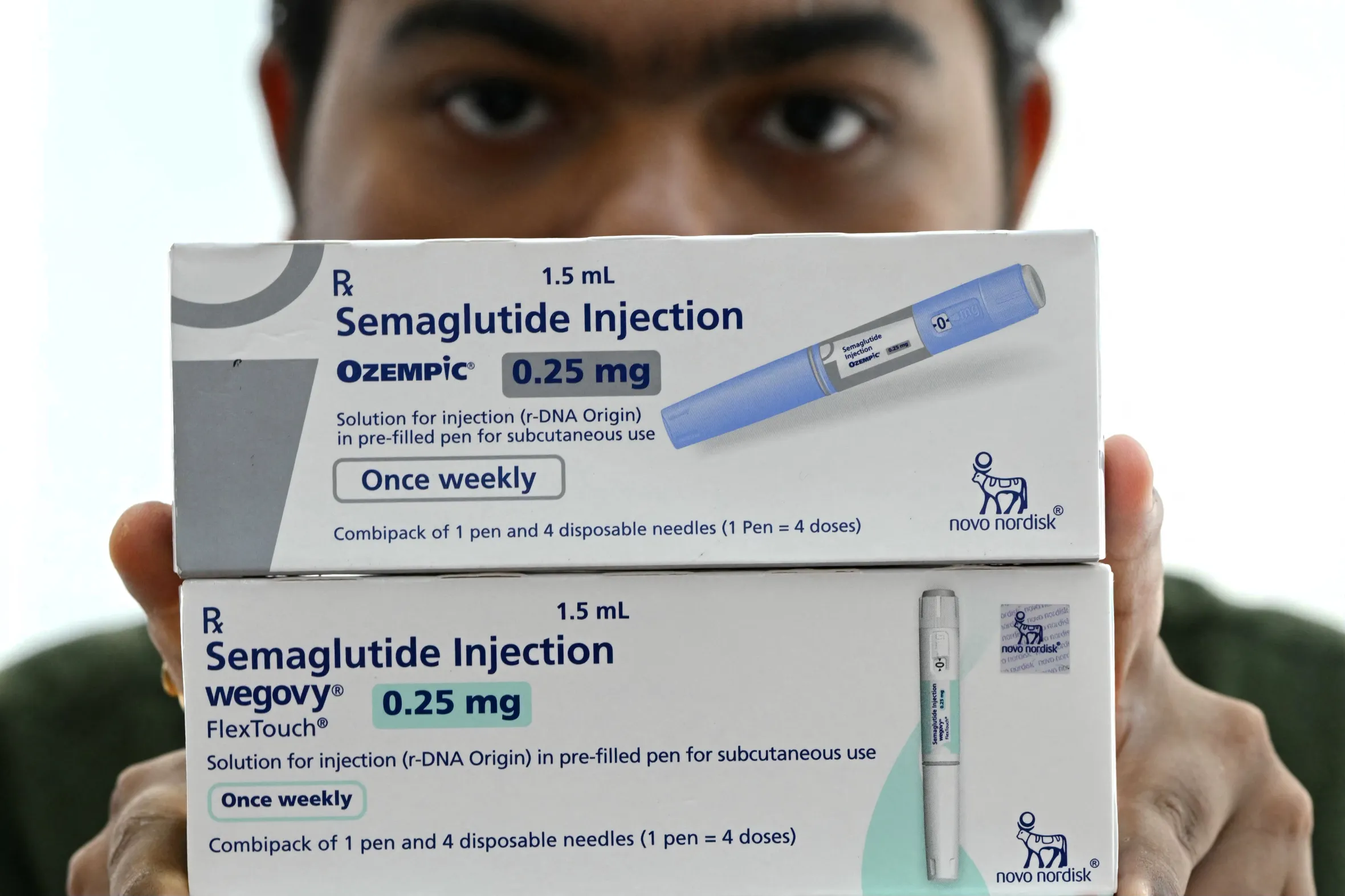 A person holding two packages of semaglutide injection pens, Ozempic and Wegovy.